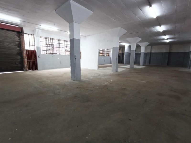 Spacious industrial utility area featuring concrete flooring, structural columns, and a large roller shutter door, suitable for storage or workshop use.