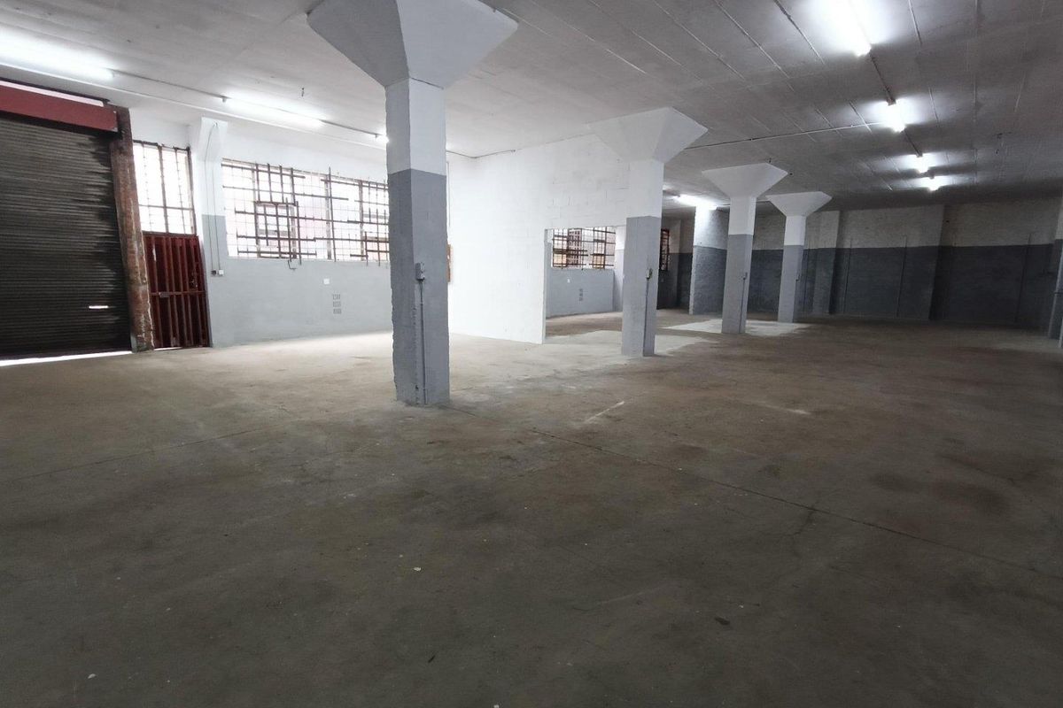 Spacious industrial utility area featuring concrete flooring, structural columns, and a large roller shutter door, suitable for storage or workshop use.