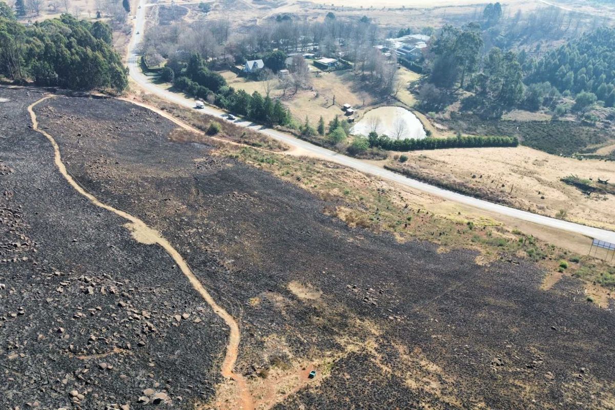 Aerial view of a large plot of land showing extensive vegetation fire damage, adjacent to a public road and rural landscape.