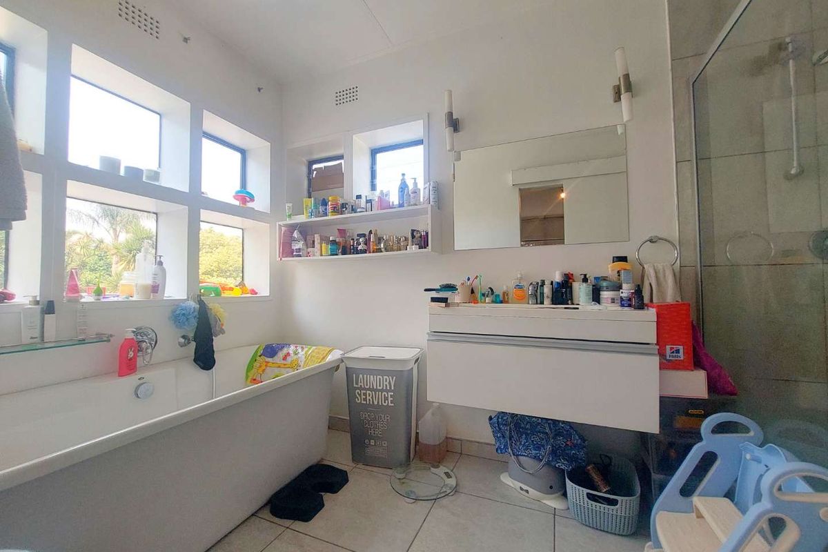 A bright bathroom featuring a freestanding bathtub, wall-mounted vanity with mirror, and a glass-enclosed shower with tiled flooring.