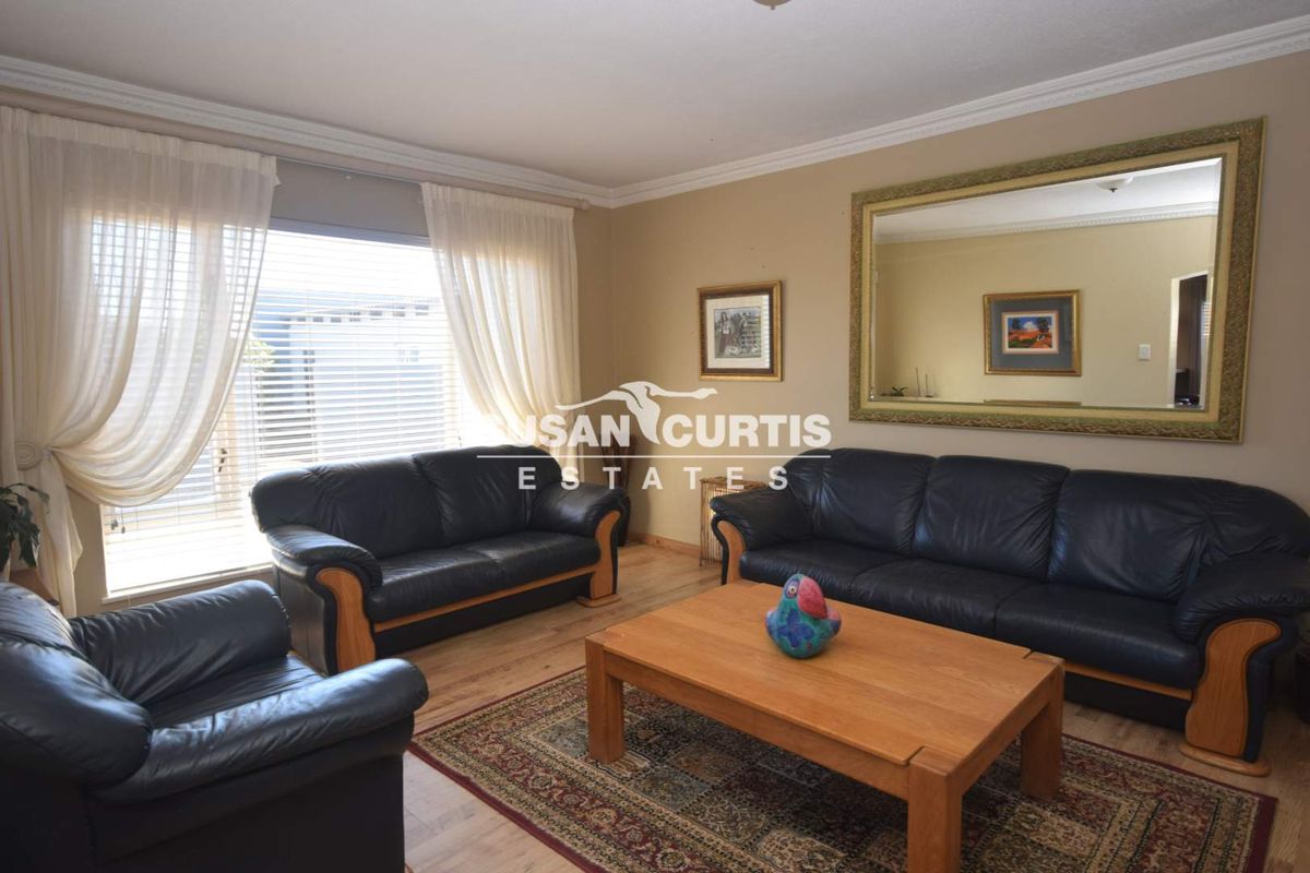 A comfortable living room featuring laminate flooring, coving, and large windows with venetian blinds, providing a bright and functional space.