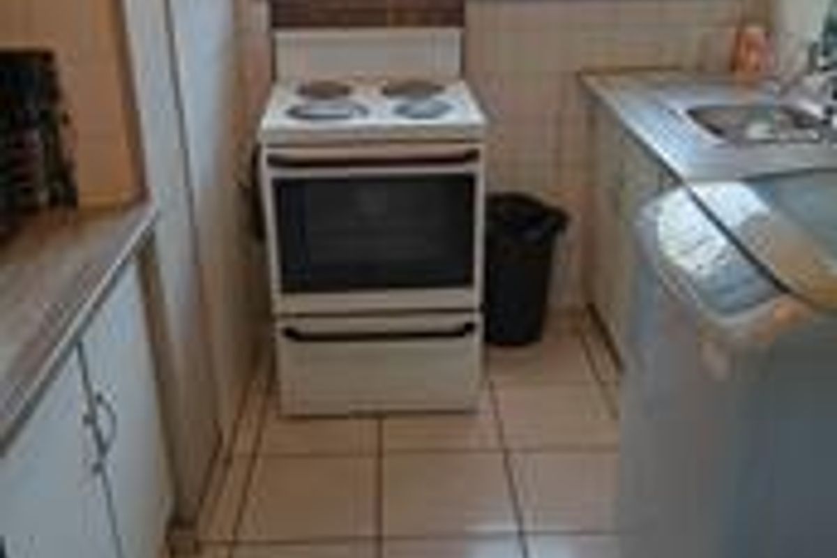 Compact kitchen featuring tiled flooring, built-in cabinetry, a freestanding electric stove, and a stainless steel sink with a window view.