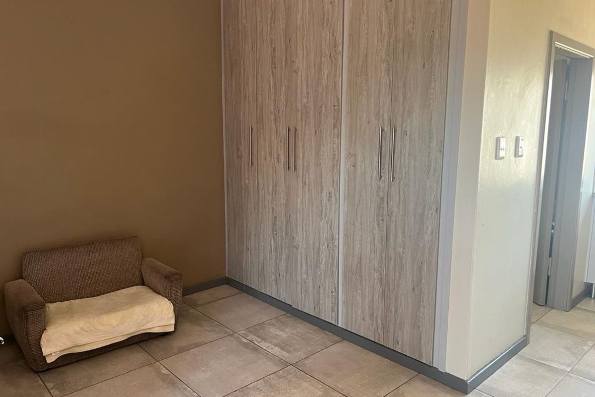 A bedroom featuring large, light wood-grain built-in cupboards and neutral floor tiling.