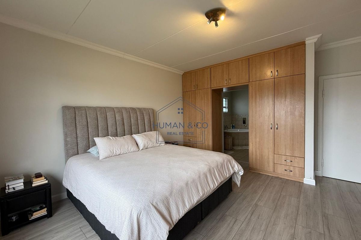 Spacious bedroom featuring built-in wooden cabinetry with integrated storage and direct access to an en-suite bathroom, finished with modern wood-look flooring.