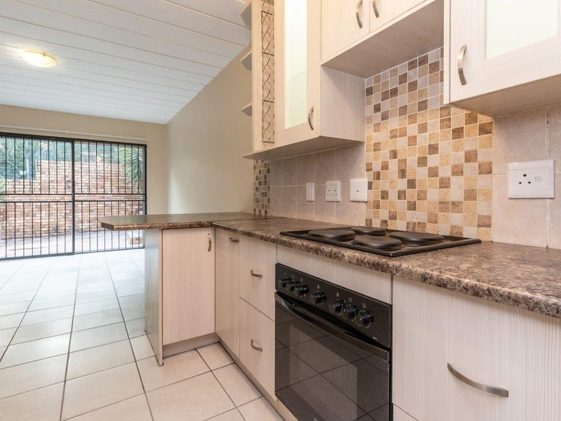 A functional kitchen featuring light wood-finish cabinetry, mosaic tile backsplash, built-in oven and hob, with direct access to an outdoor patio area.
