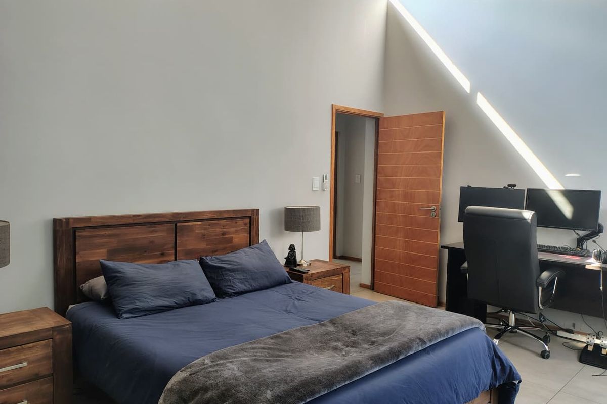 Spacious bedroom featuring high raked ceilings with clerestory windows, tiled flooring, and a solid timber door leading to the hallway.