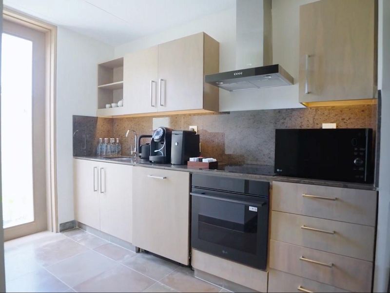 Modern kitchen featuring light wood cabinetry, stone countertops, integrated appliances including an oven and extractor fan, and tiled flooring with access to an outdoor area.