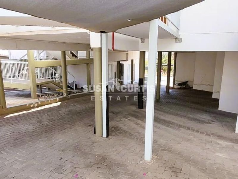 A covered parking area featuring paved ground, steel support columns, and an adjacent staircase leading to the apartment levels.