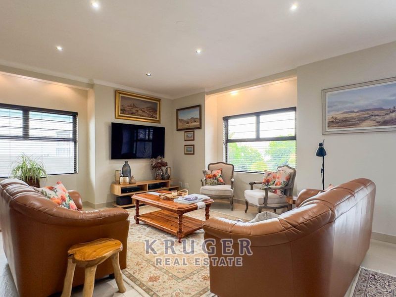 A well-lit living room featuring tiled flooring, recessed downlighting, and large windows with aluminium frames, creating a bright and comfortable space.