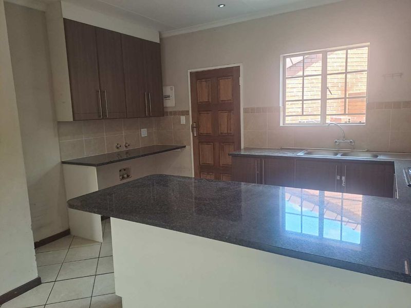 A functional kitchen featuring granite countertops, ample built-in cabinetry, a double basin sink, and tiled flooring, offering a clean and practical workspace.