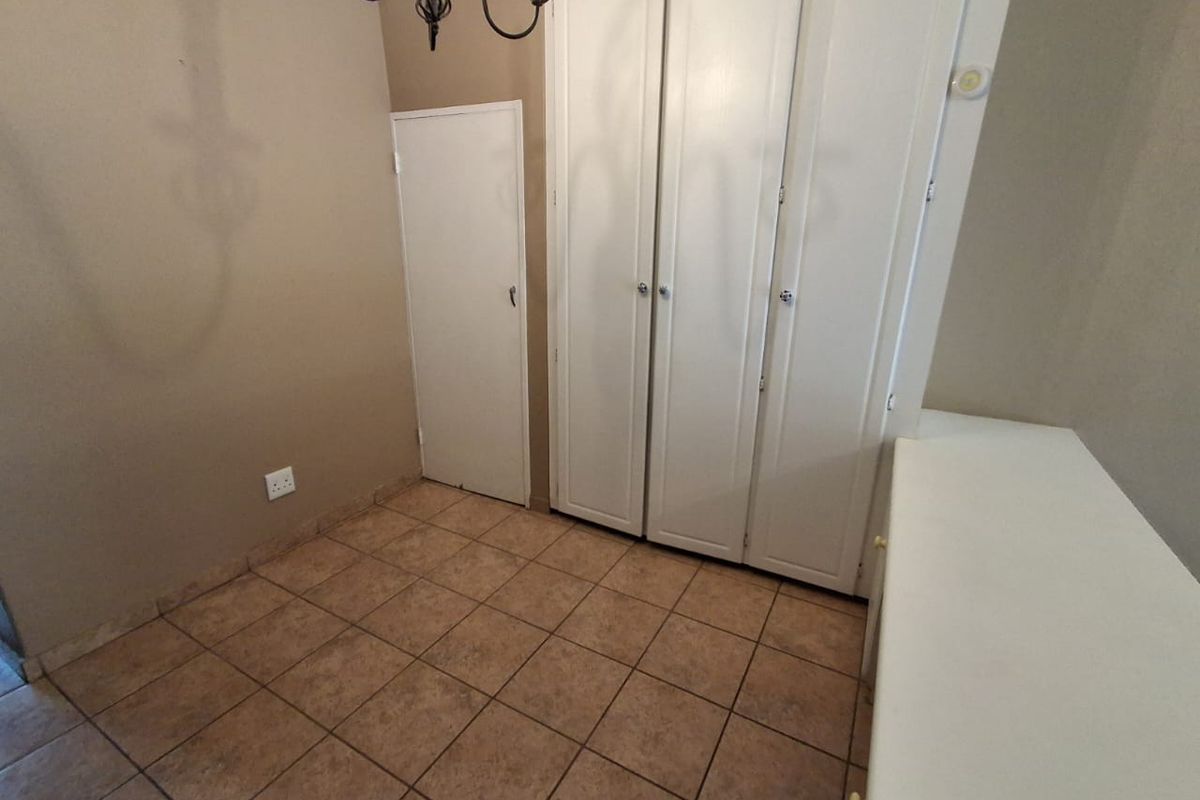 A bedroom featuring built-in cupboards, tiled flooring, and neutral wall tones, offering a functional and clean living space.