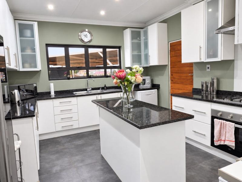 Modern kitchen featuring white cabinetry, dark granite countertops, a central island, built-in oven, hob, and extractor fan with tiled flooring.