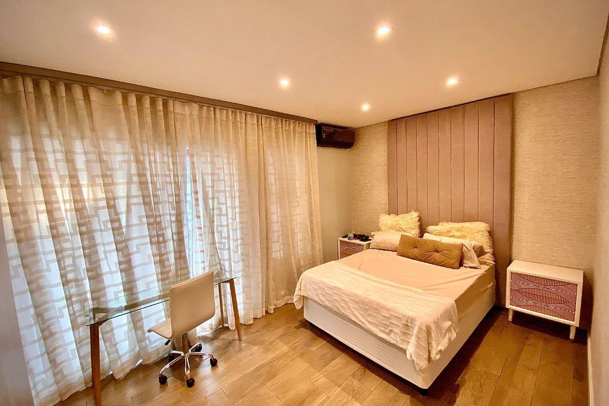 A well-maintained bedroom featuring recessed ceiling lighting, wood-look flooring, and a large upholstered headboard wall panel.