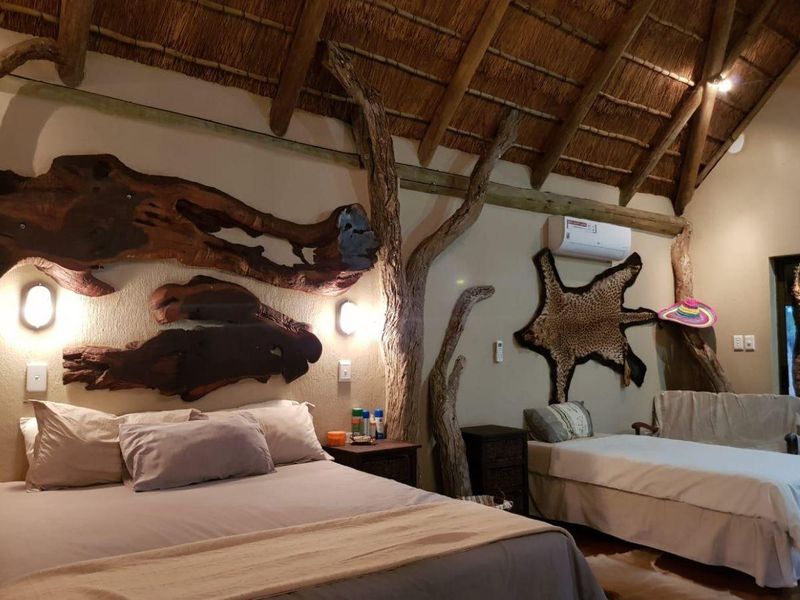 A rustic bedroom featuring a high thatched roof with exposed timber rafters, textured walls, and a built-in air conditioning unit.