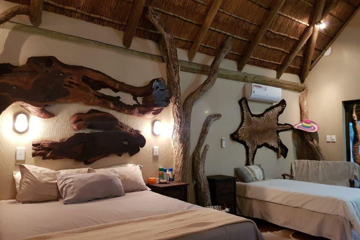 A rustic bedroom featuring a high thatched roof with exposed timber rafters, textured walls, and a built-in air conditioning unit.