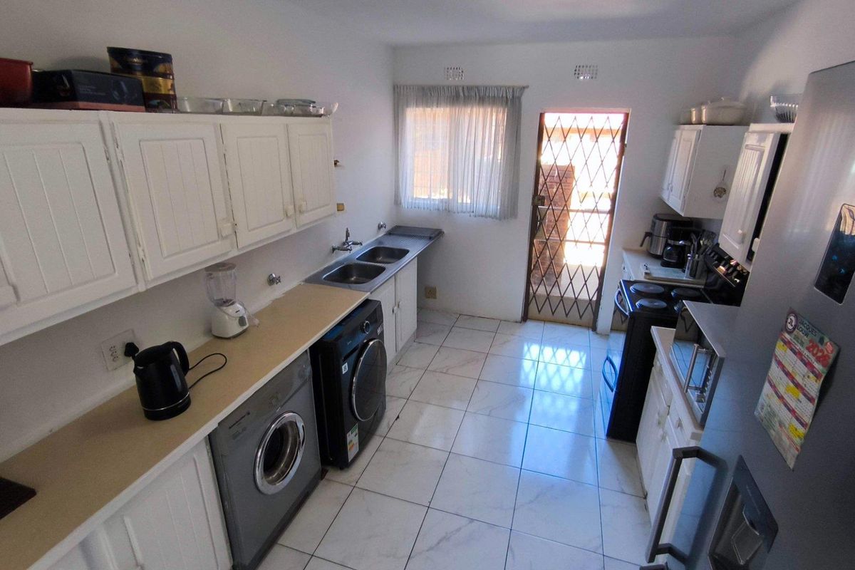 A functional kitchen featuring white cabinetry, tiled flooring, a double sink, and direct access to an exterior security gate.