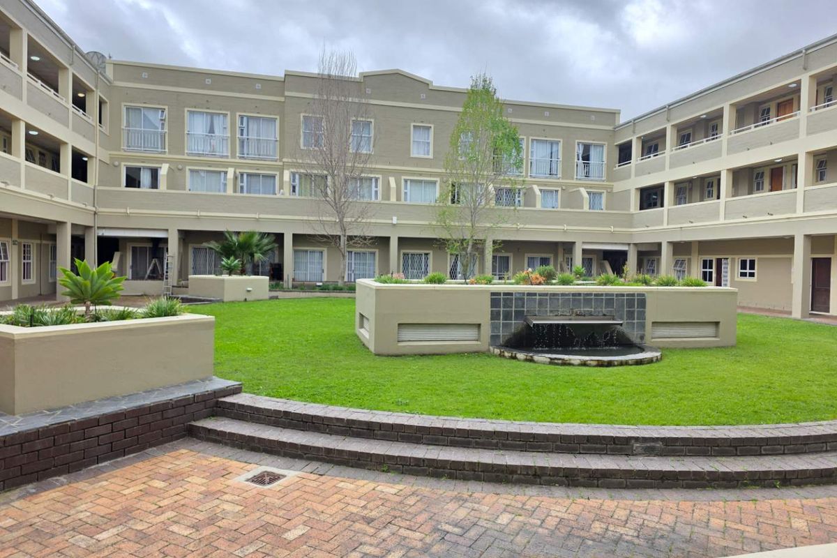 A well-maintained central courtyard area featuring a water fountain, manicured lawn, brick paving, and surrounding multi-story apartment building facades.