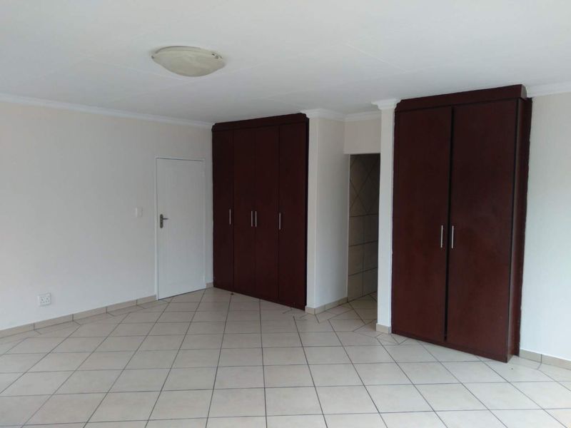 Spacious bedroom featuring neutral tiled flooring and extensive dark wood built-in cupboards, offering a clean and functional layout.
