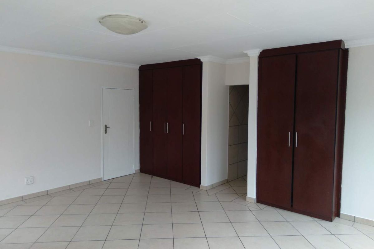 Spacious bedroom featuring neutral tiled flooring and extensive dark wood built-in cupboards, offering a clean and functional layout.