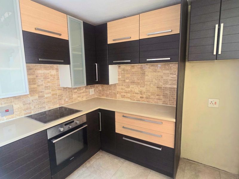 Modern kitchen featuring two-tone cabinetry, stone countertops, mosaic tile backsplash, and integrated electric hob and oven.
