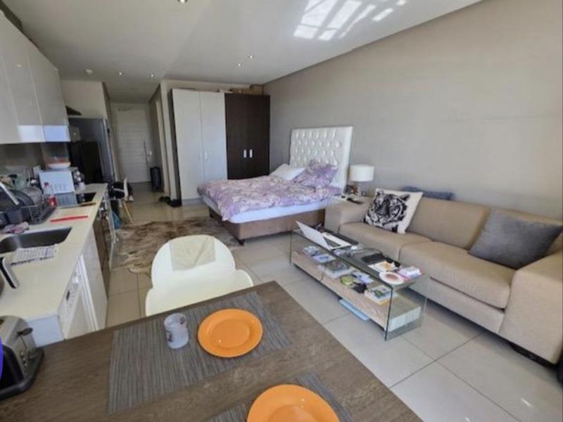 An open-plan studio apartment featuring a compact kitchen with built-in cabinetry, tiled flooring, and recessed lighting, seamlessly integrating living and sleeping areas.