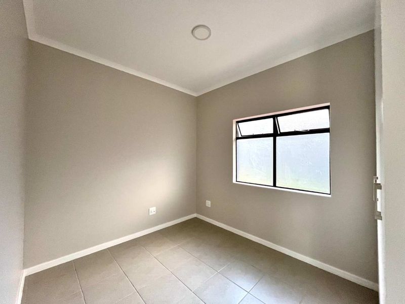A clean, empty bedroom featuring neutral wall tones, tiled flooring, and an aluminium-framed window, providing a versatile space ready for personalization.