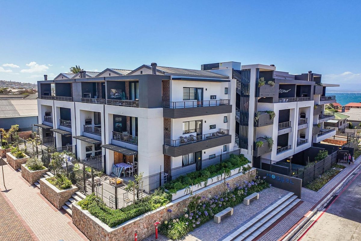 Aerial view of a modern multi-story apartment complex featuring contemporary architecture, private balconies, and landscaped ground-level garden areas.