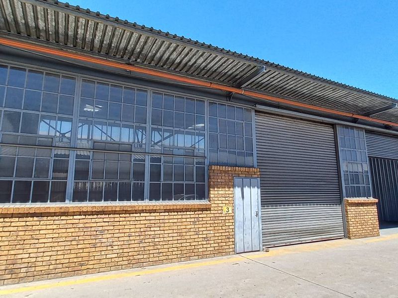 Industrial warehouse exterior featuring a brick facade, large steel-framed windows, and a roller shutter door with a concrete apron.