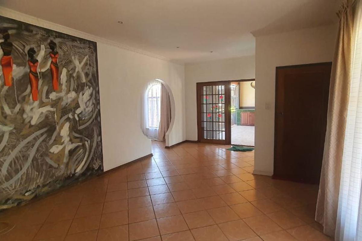 Spacious living area featuring ceramic floor tiles, an arched window, and a glass-paneled door leading to an outdoor patio space.