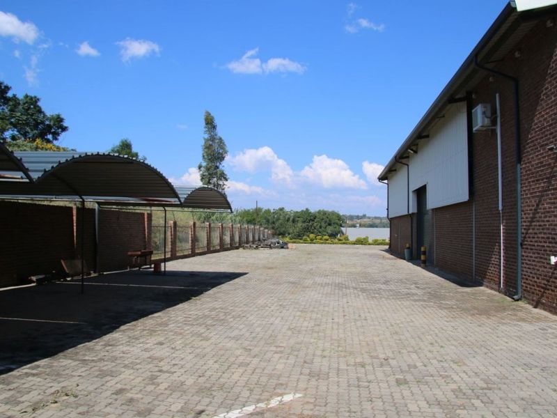 Spacious industrial rear yard featuring paved driveway, covered parking bays, and brick boundary walls with access to the main warehouse structure.