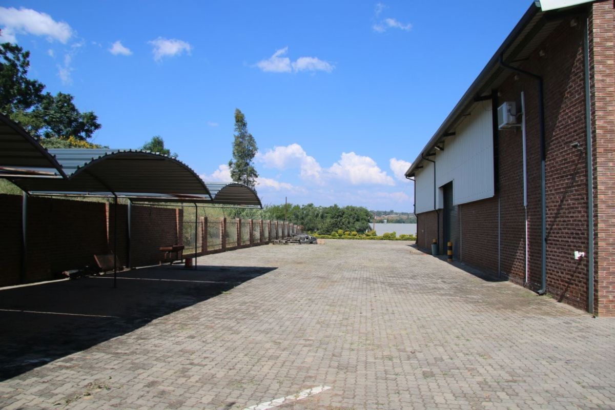 Spacious industrial rear yard featuring paved driveway, covered parking bays, and brick boundary walls with access to the main warehouse structure.