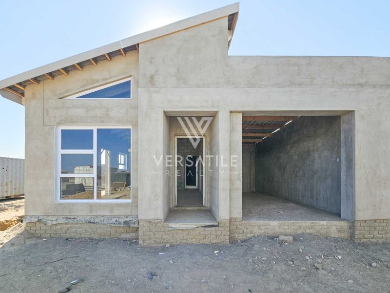 Front elevation of a townhouse under construction, featuring raw concrete walls, aluminium windows, and an unfinished entrance and garage area.