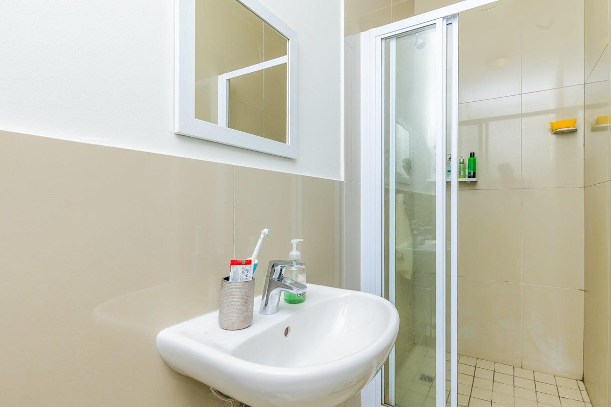 A functional bathroom featuring a wall-mounted basin, a framed mirror, and a glass-enclosed shower with tiled walls and flooring.