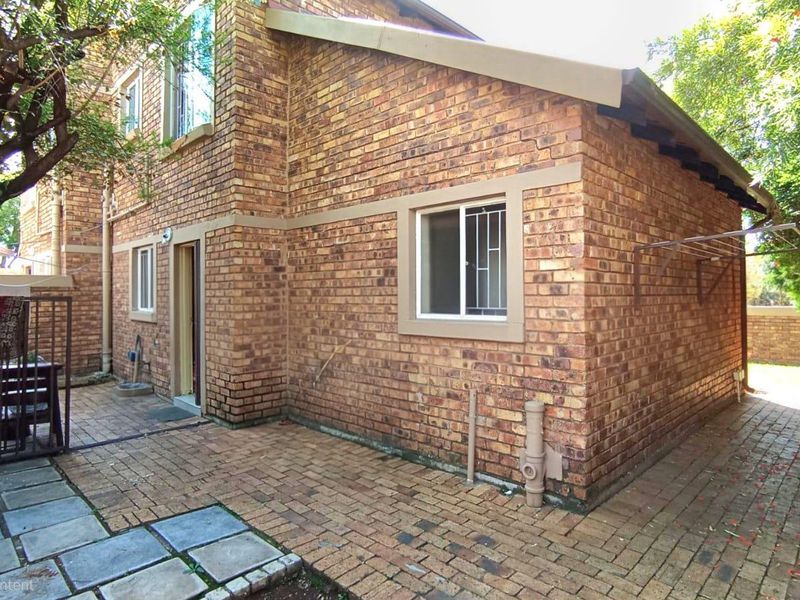Rear exterior view of the townhouse featuring a face brick facade, paved patio area, and secure window fittings.