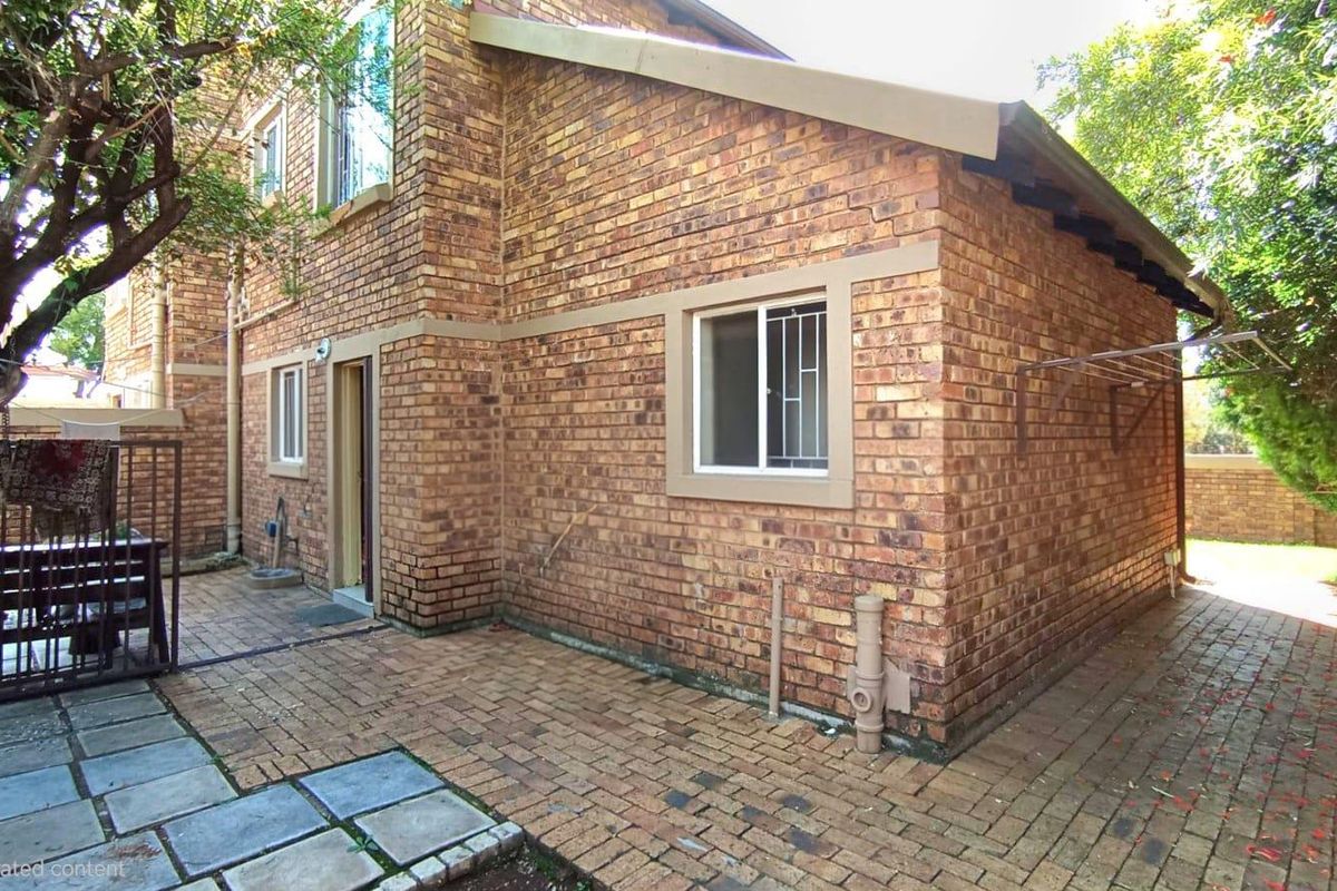 Rear exterior view of the townhouse featuring a face brick facade, paved patio area, and secure window fittings.