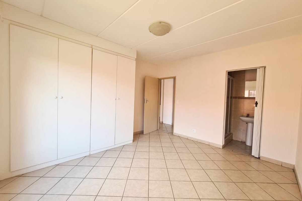 A spacious bedroom featuring built-in cupboards, tiled flooring, and an en-suite bathroom with a shower.
