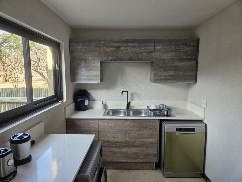A functional scullery featuring modern wood-look cabinetry, stone countertops, a double basin sink with a black mixer tap, and a large sliding window.