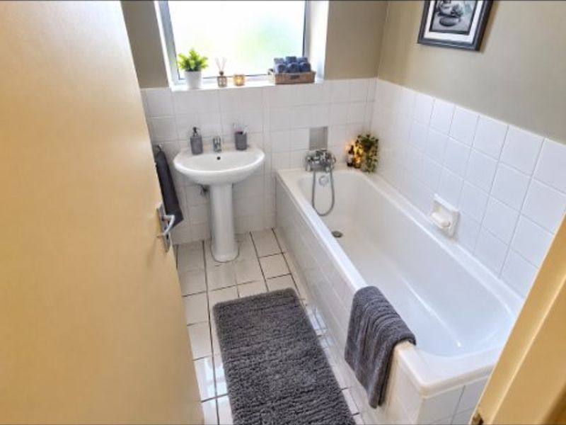 A functional bathroom featuring a white pedestal basin, bathtub with shower mixer, and tiled walls and flooring.
