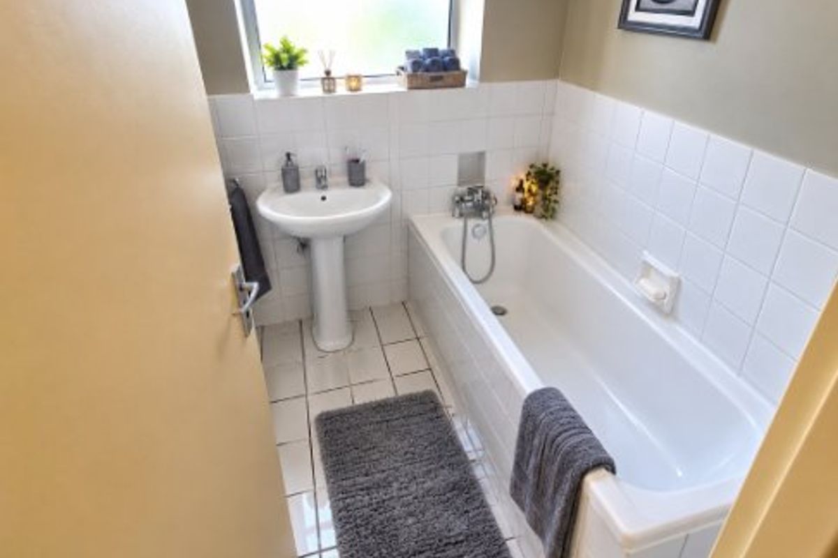 A functional bathroom featuring a white pedestal basin, bathtub with shower mixer, and tiled walls and flooring.