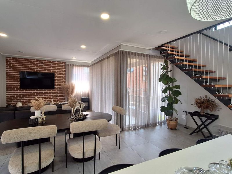 Modern open-plan living and dining area featuring an exposed brick wall, tiled flooring, and a contemporary staircase with timber treads and cable balustrade.