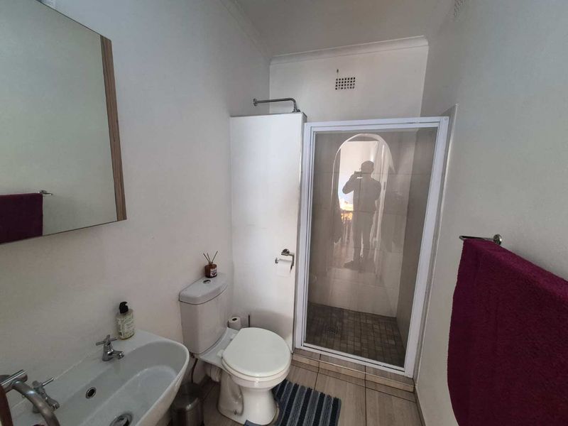 A functional bathroom featuring a shower enclosure, pedestal basin, and toilet with neutral tiled flooring and wall-mounted mirror.