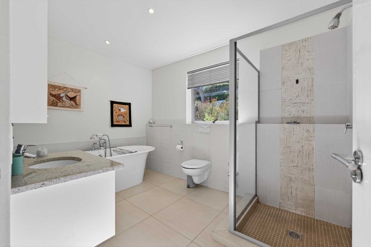 A bright, modern bathroom featuring a freestanding bathtub, a separate walk-in shower with tiled accents, a wall-mounted toilet, and a granite-topped vanity.