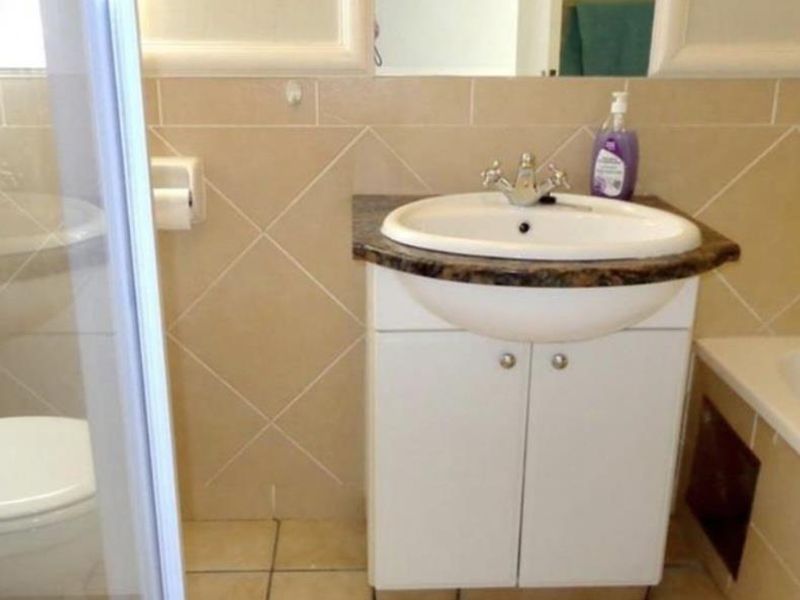 A functional bathroom featuring a vanity cabinet with a basin, tiled splashback, tiled flooring, and a glass shower enclosure.