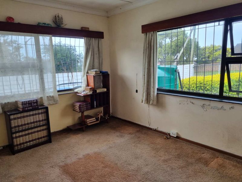 A bedroom featuring carpet flooring, security bars on windows, and visible wall plaster damage requiring maintenance and cosmetic updates.