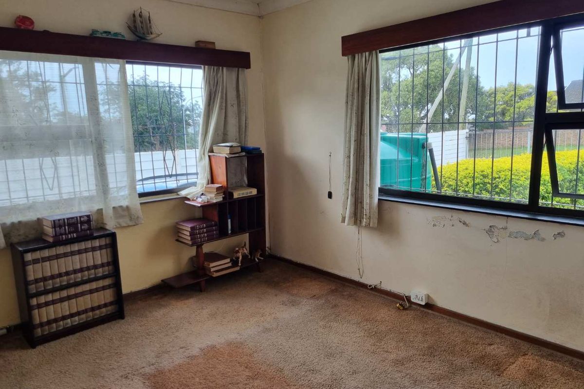 A bedroom featuring carpet flooring, security bars on windows, and visible wall plaster damage requiring maintenance and cosmetic updates.