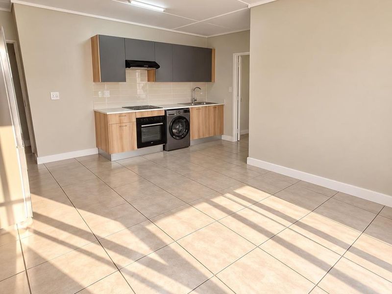 A bright, open-plan living and kitchen area featuring modern two-tone cabinetry, integrated appliances, and neutral tiled flooring throughout.