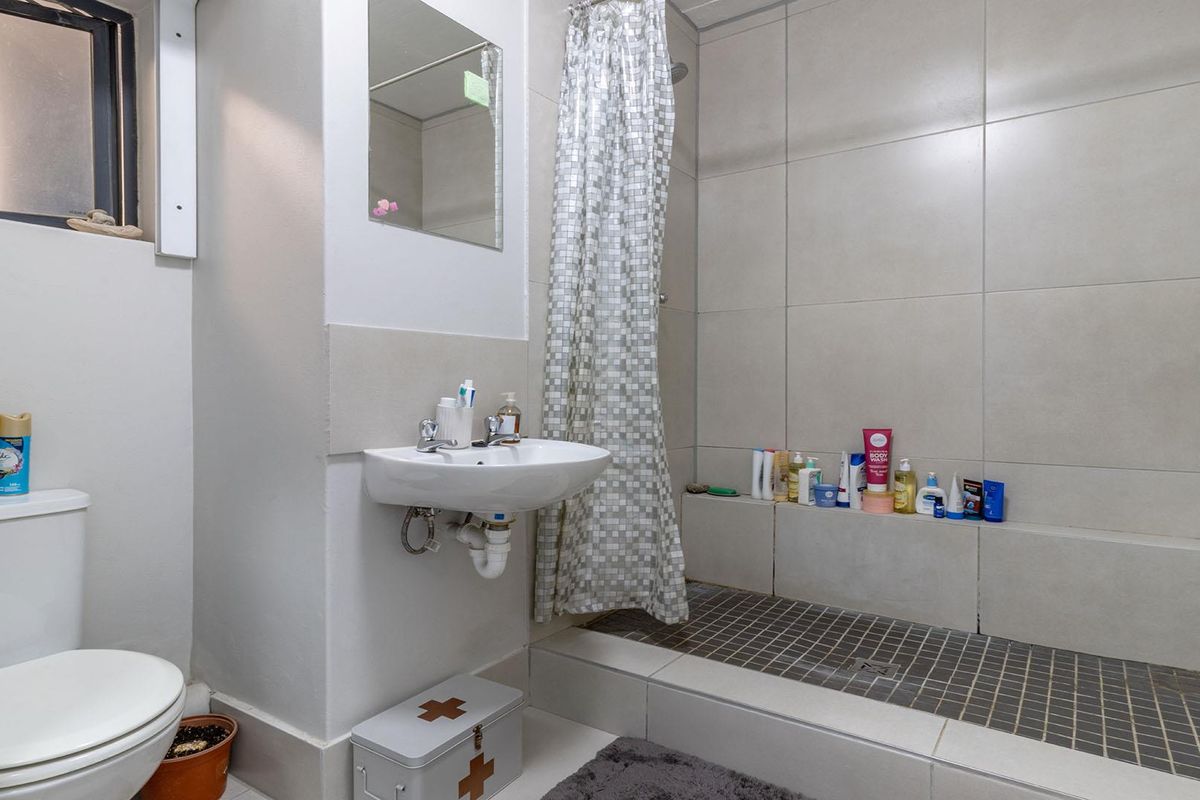A functional bathroom featuring a walk-in shower with tiled walls, a wall-mounted basin, and a standard toilet.