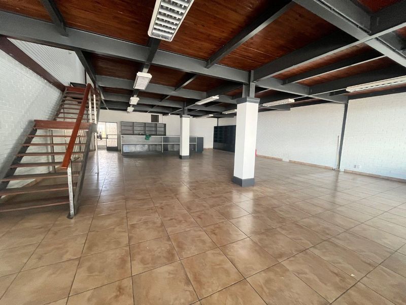 Spacious open-plan commercial area featuring exposed steel beams, timber ceilings, tiled flooring, and a built-in counter with an internal staircase.
