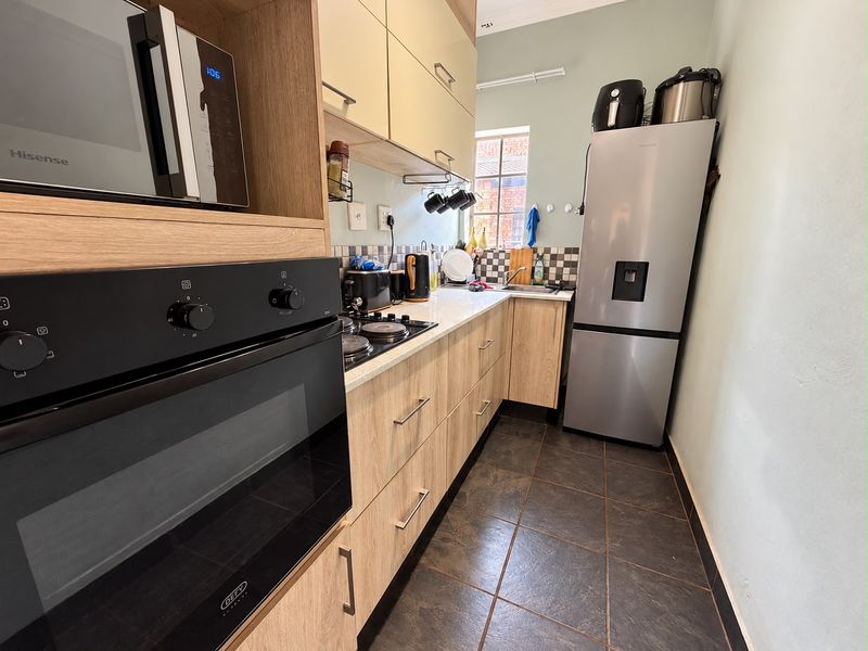 A functional galley-style kitchen featuring light wood-finish cabinetry, a built-in oven, hob, and tiled flooring, offering efficient workspace and storage.