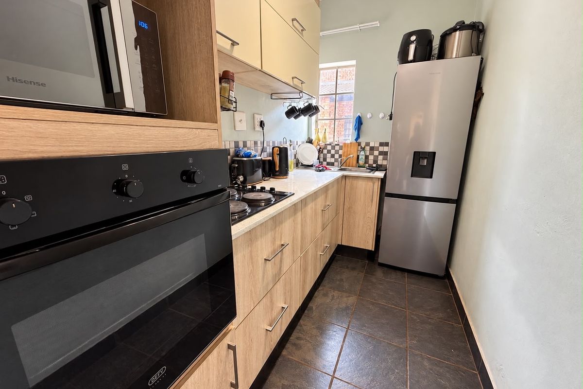 A functional galley-style kitchen featuring light wood-finish cabinetry, a built-in oven, hob, and tiled flooring, offering efficient workspace and storage.